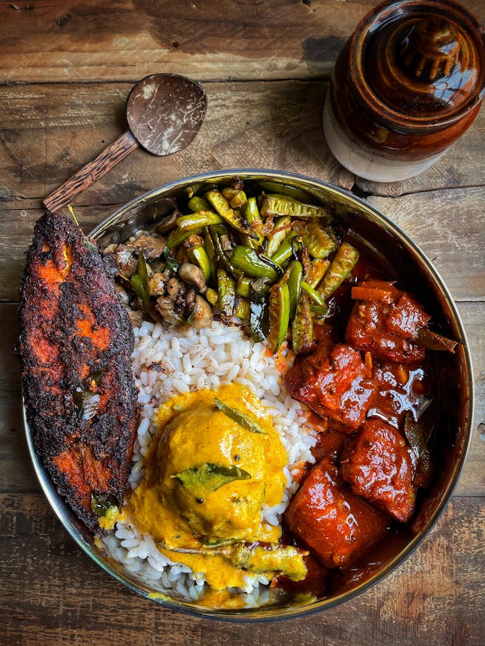 Delicious Indian meal featuring rice, curry, vegetables, and fried fish on a rustic wooden table.