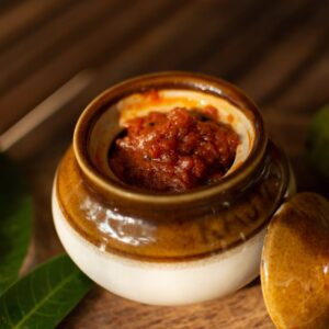 Traditional Indian mango pickle in a rustic ceramic jar on a wooden surface, perfect for food lovers.